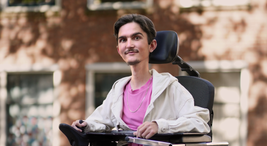 Endri, bekend als Lilhandi op TikTok, lacht naar de camera in zijn elektrische rolstoel