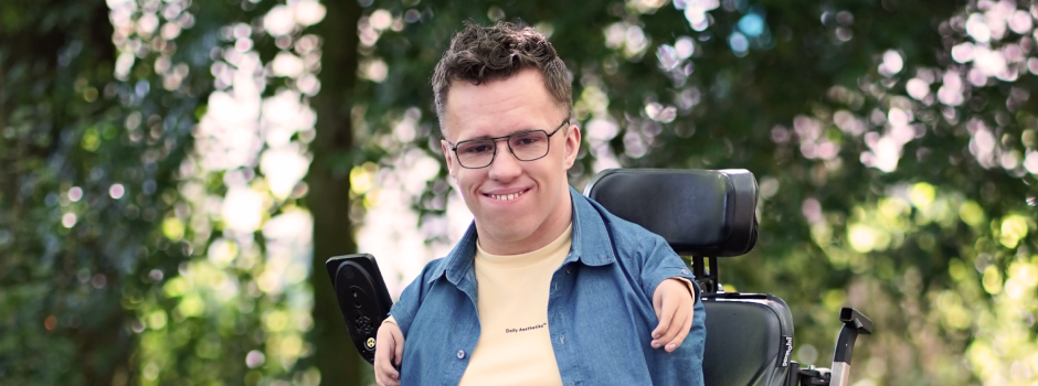 Glenn buiten in zijn elektrische rolstoel, lachend naar de camera