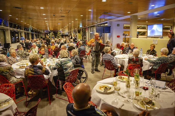 Tijdens het kerstdiner dat Amgen organiseerde voor 150 deelnemers van de Zonnebloem uit de regio Breda, was accordeonist Hans de Cock aanwezig om bekende nummers te spelen