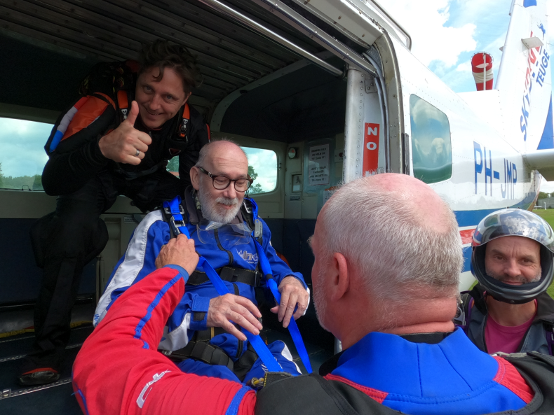 Mark wordt in het vliegtuig getild door de begeleiders