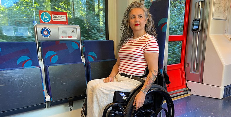 Max de Bruin in haar rolstoel in het openbaar vervoer, op een plaats voor gehandicapten.