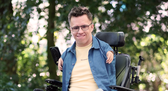 Glenn zit in zijn elektrische rolstoel en lacht naar de camera